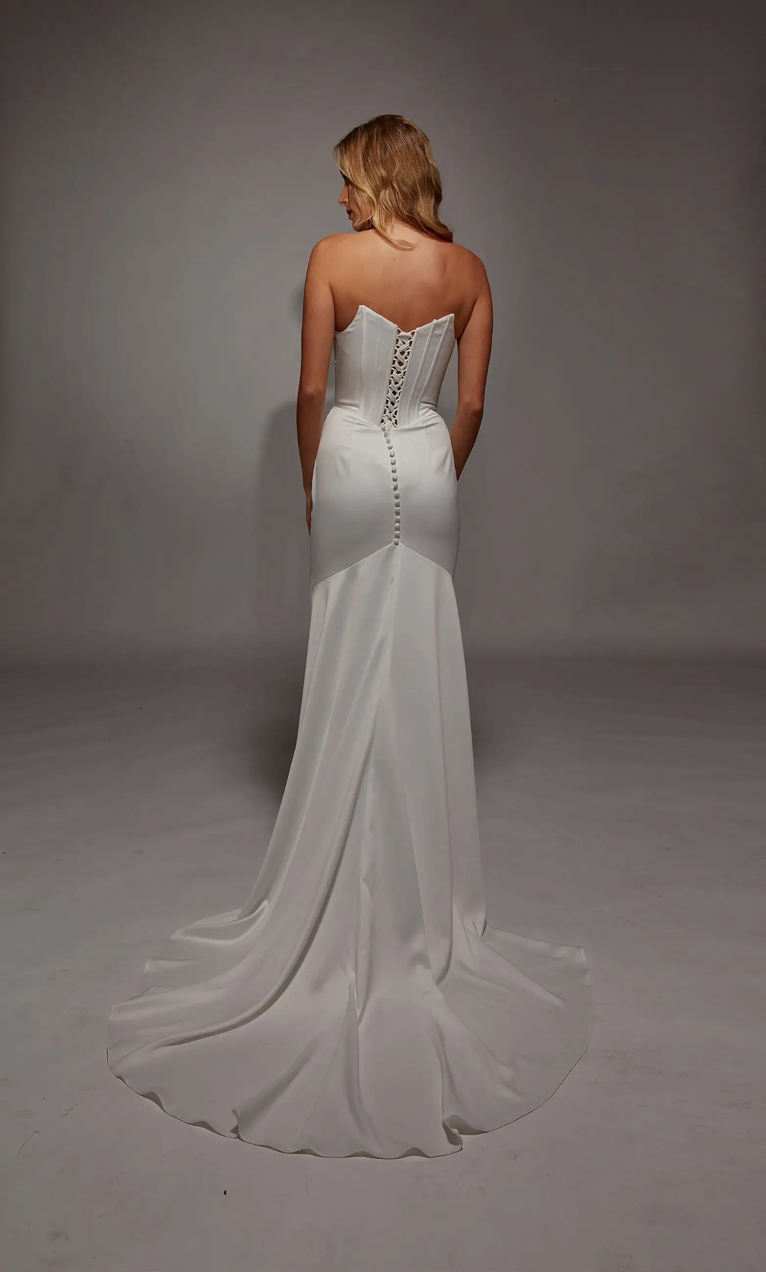 Model is wearing a sheath strapless wedding dress with a basque waist and sleek fabric