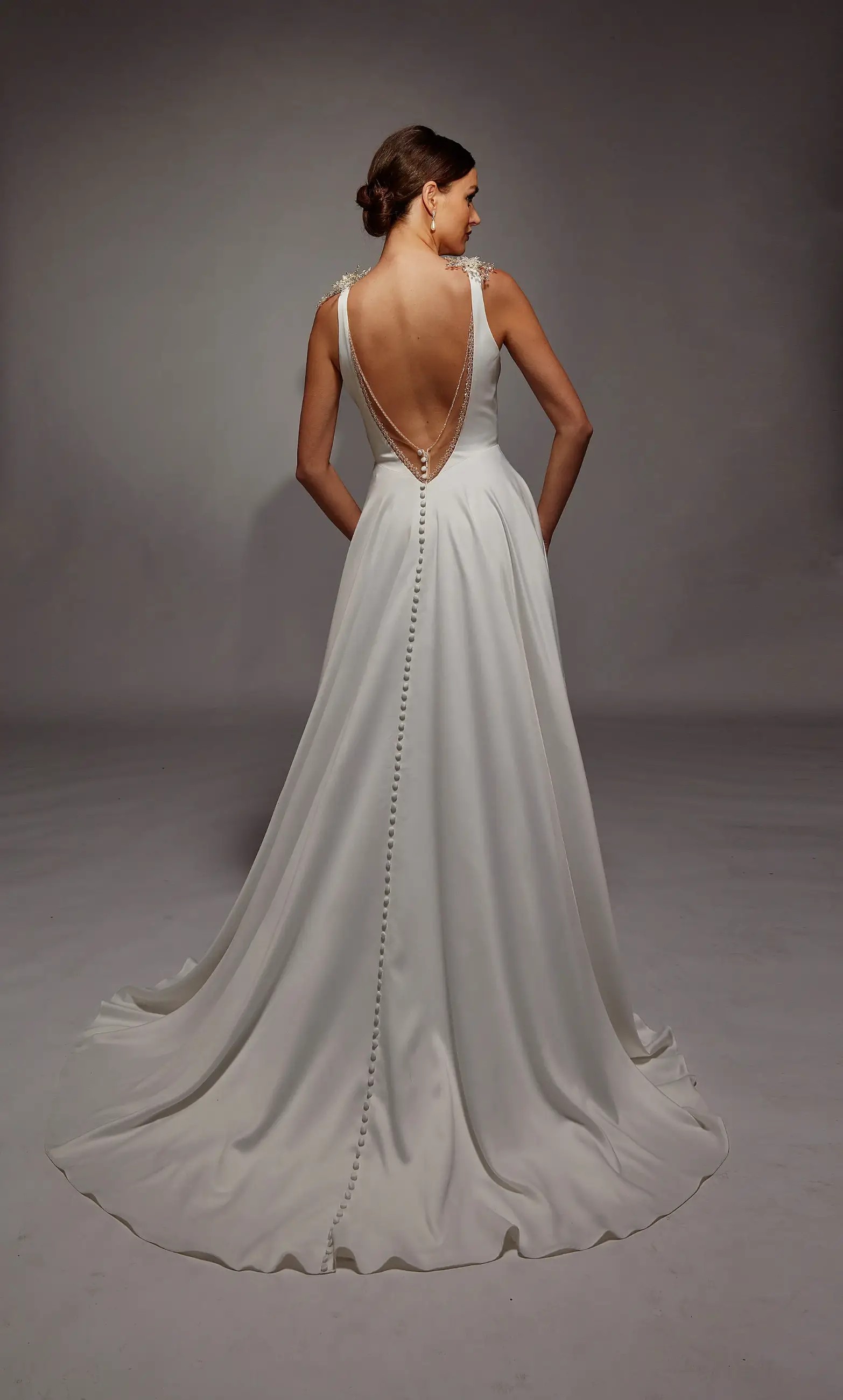 Model is wearing an a-line sleeveless wedding gown with plunging neckline and open back