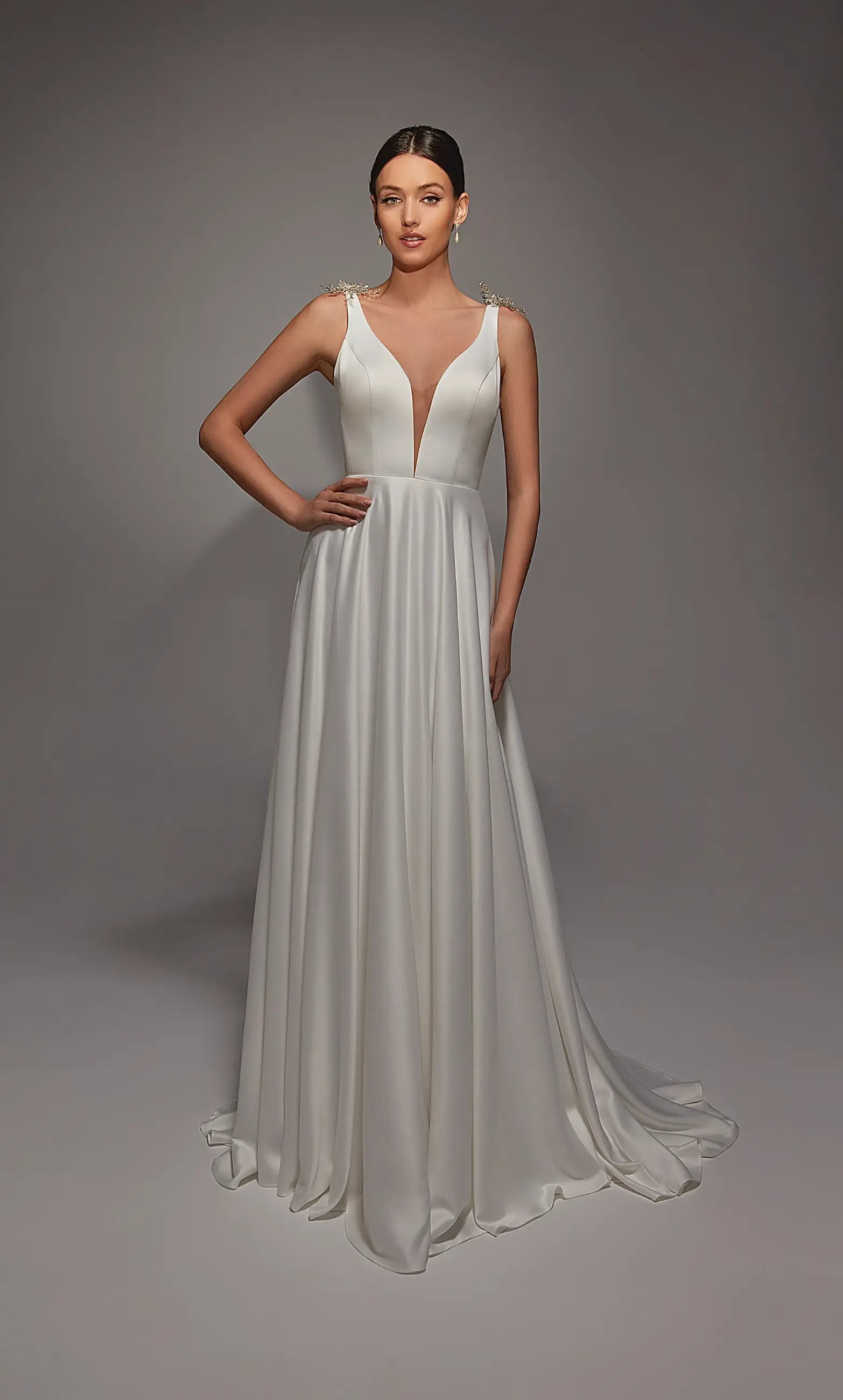 Model is wearing an a-line sleeveless wedding gown with plunging neckline and open back