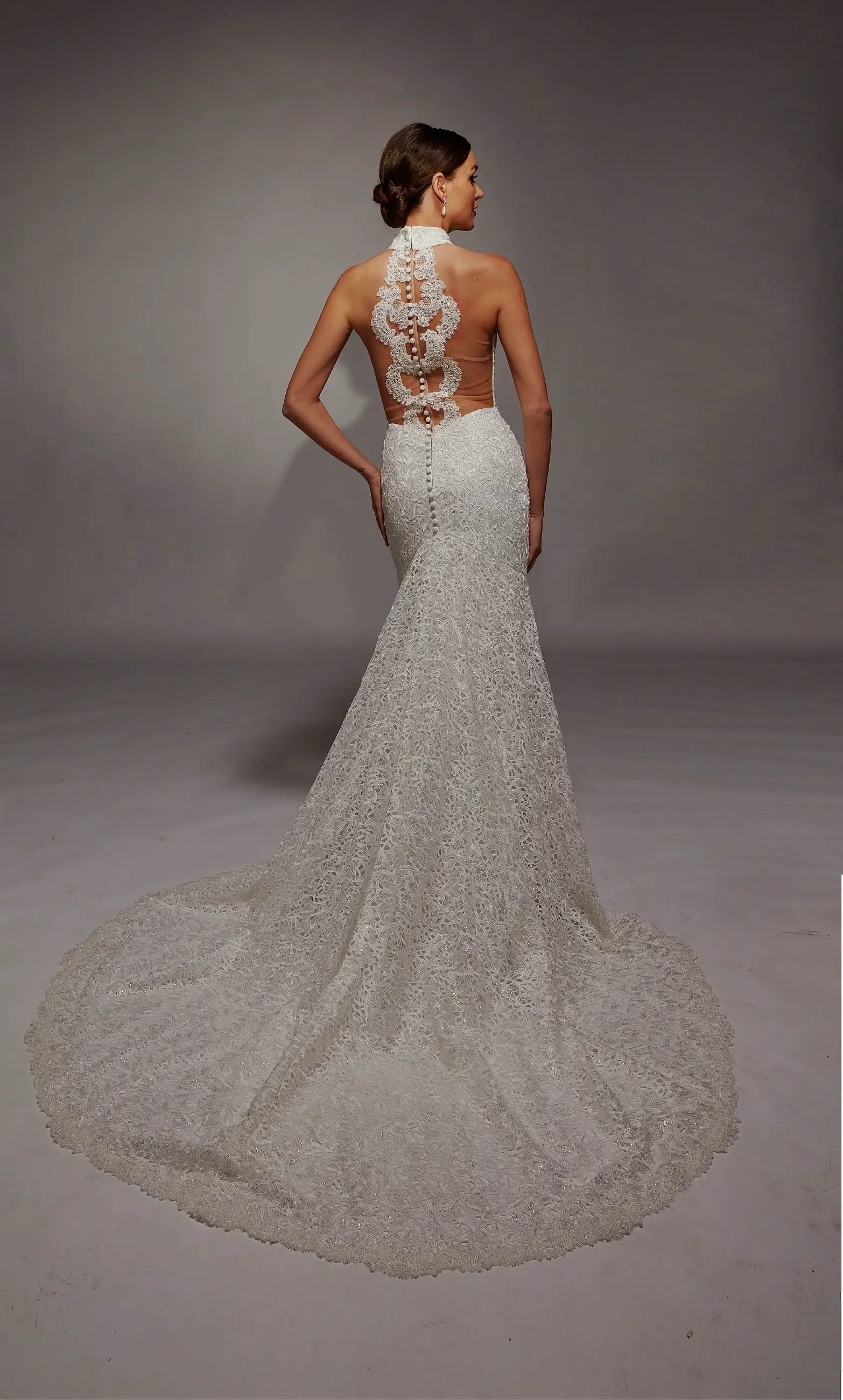 Model is wearing a glamorous fit and flare wedding dress with a halter inspired neck, sleeveless, and covered in beadwork with an elaborate lace back