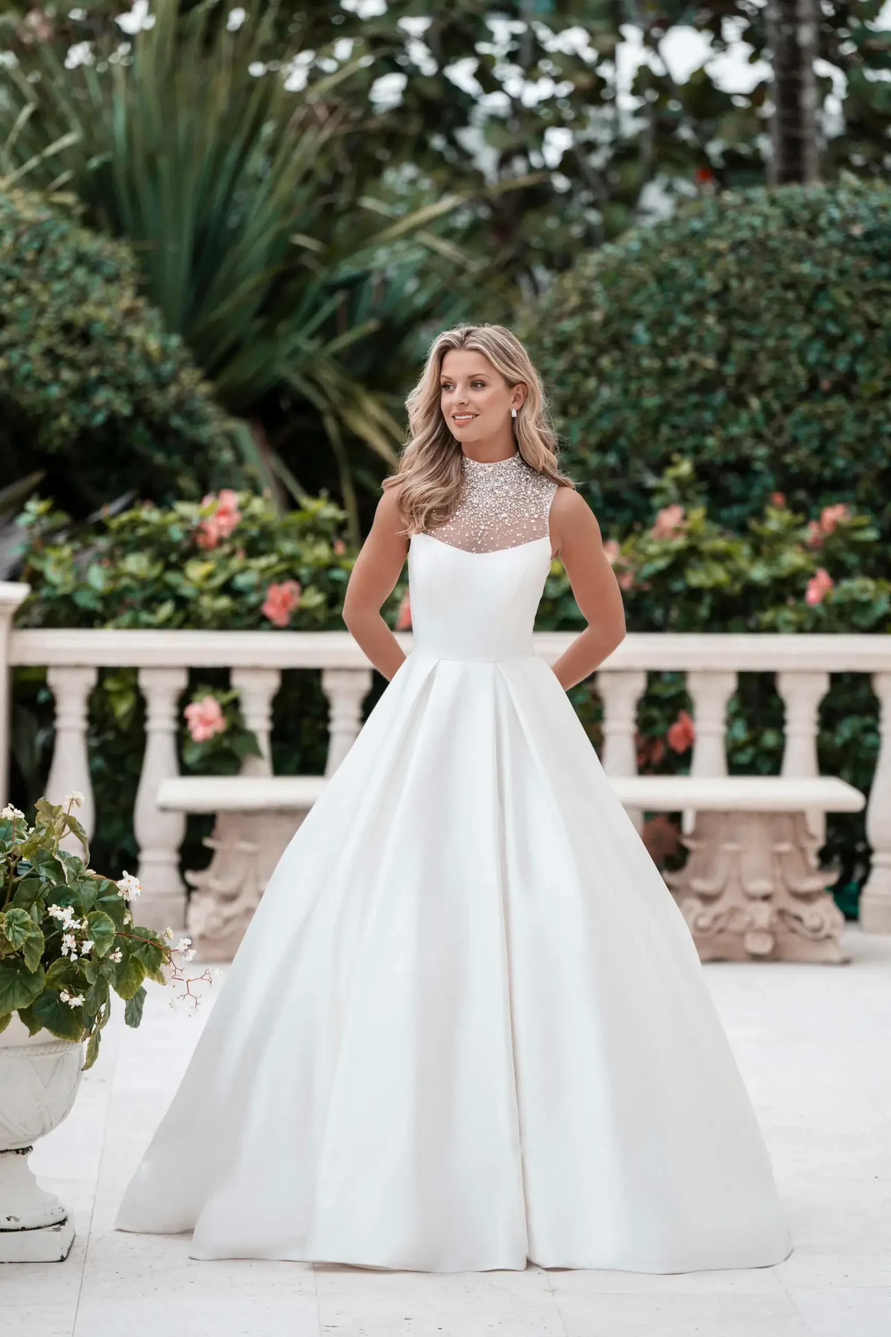 Model is wearing a sleek mikado ball gown with a regal high neckline, pearl button details, and optional matching sleeves.