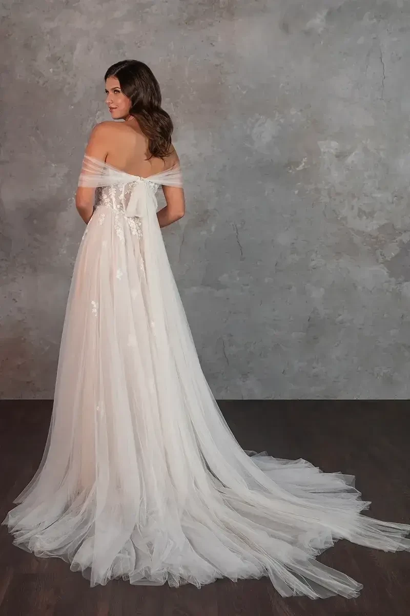 Model is wearing a soft tulle gown with a sweetheart neckline, high leg slit, and a stunning open back with floral appliques.