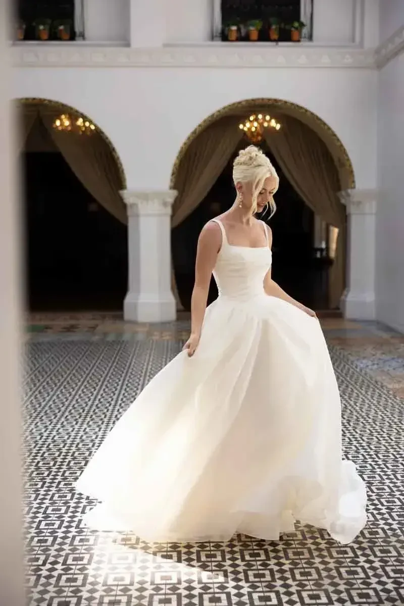 A bride in a white wedding dress gracefully poses in an elegant indoor setting with archways and decorative lighting.