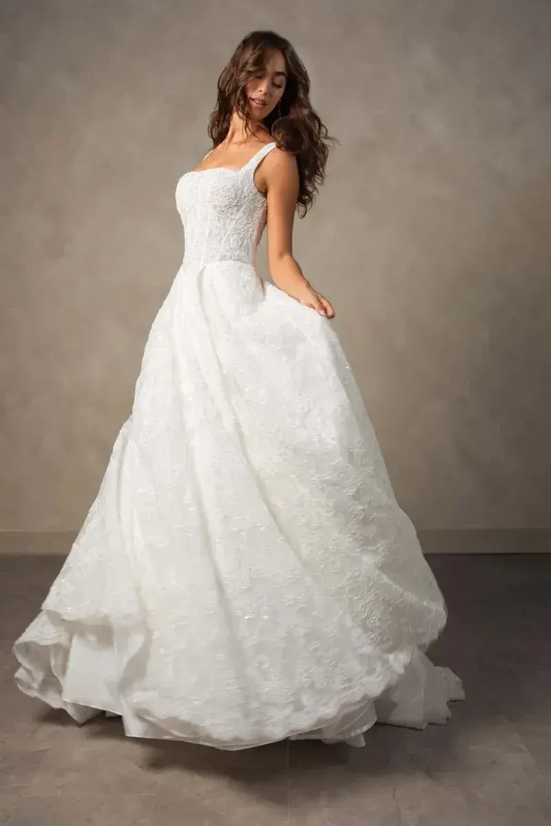 A woman in a flowing white wedding dress stands, gracefully twirling with the skirt of her dress billowing around her.