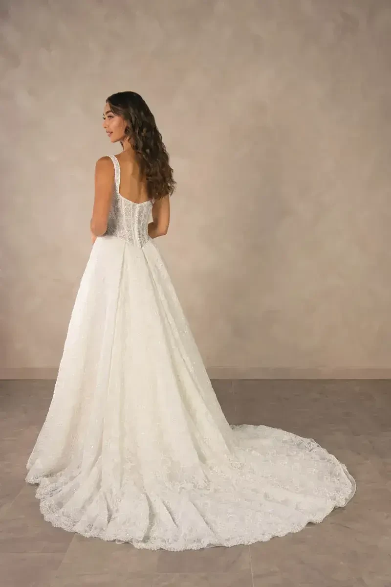 A woman in a white wedding dress, viewed from the back, standing against a neutral background.