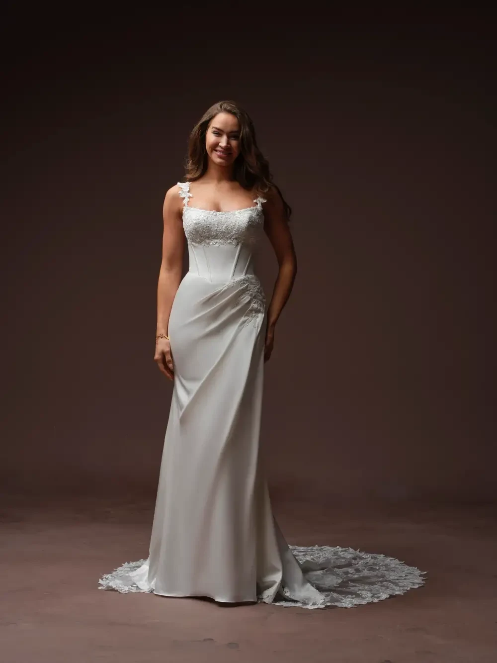 A woman in a white wedding dress with lace details, standing against a dark background.