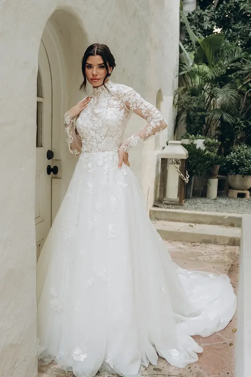 Model is wearing a romantic ball gown with a high neckline, sheer bodice, and an open lace keyhole back for a dramatic finish.