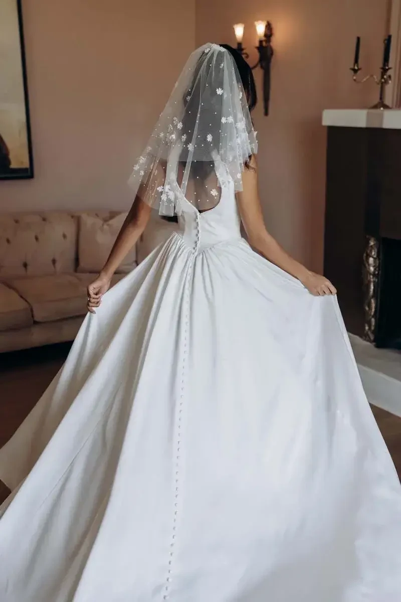 A person wearing a white wedding dress and a veil, standing in a room with muted colors and elegant decor.